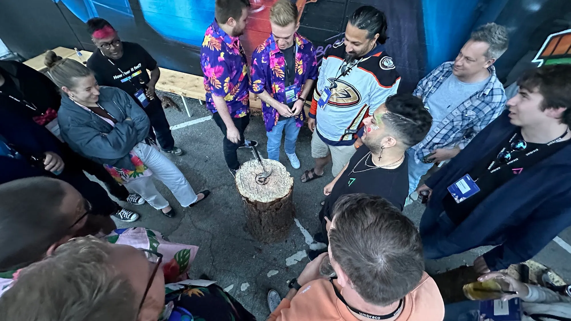 A circle of community members stood around a tree stump playing hammerschlagen