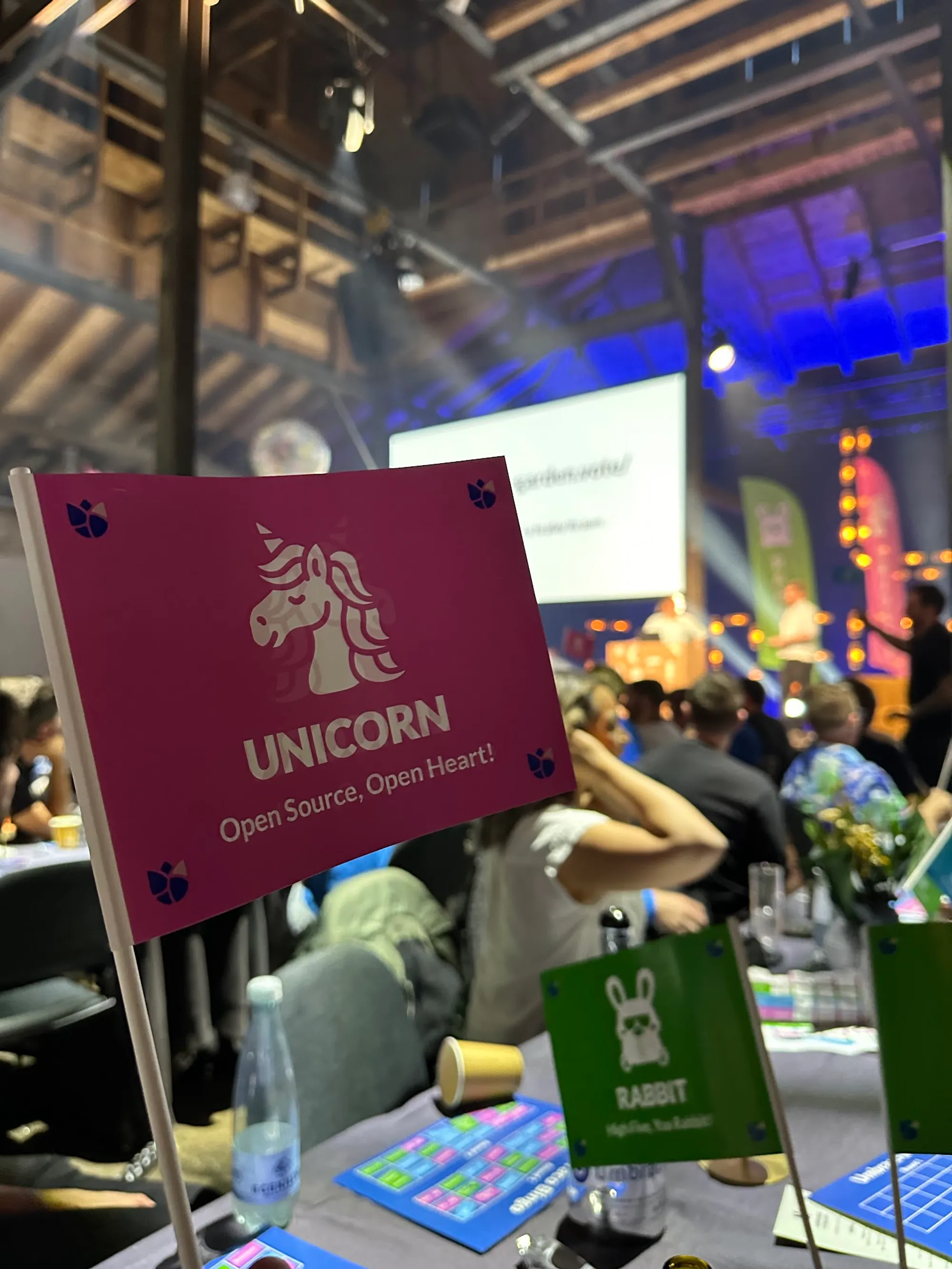 A pink flag with an illustration of a unicorn, reading "Unicorn. Open source, open heart!". In the background is the Codegarden conference out of focus